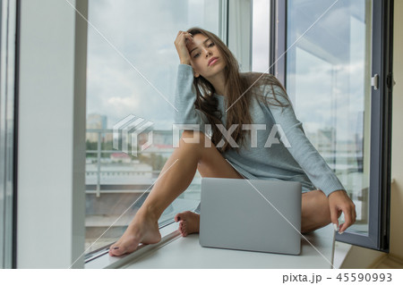 Beautiful young woman sitting on the windowsill with a laptop. 45590993