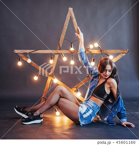 Sexy brunette woman in nice jeans in the studio. Wooden star with lights on a black background Sexy brunette woman in nice jeans in the studio. Wooden star with lights on a black background 45601160