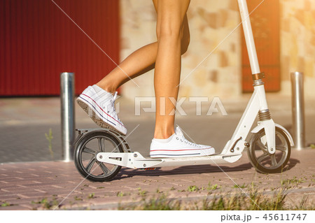 Beautiful girl riding a scooter down the street Beautiful girl riding a scooter down the street 45611747
