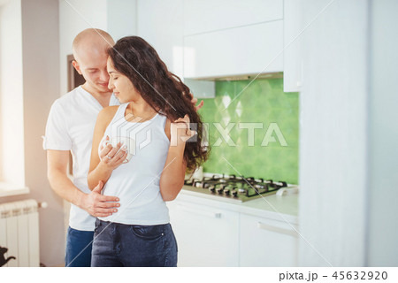 Beautiful young couple is talking, looking at camera and smiling while cooking in kitchen. Beautiful young couple is talking, looking at camera and smiling while cooking in kitchen. 45632920