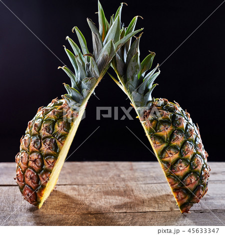Tropical ripe fruit pineapple with green leaves presented on a wooden table around a dark background Tropical ripe fruit pineapple with green leaves presented on a wooden table around a dark background 45633347