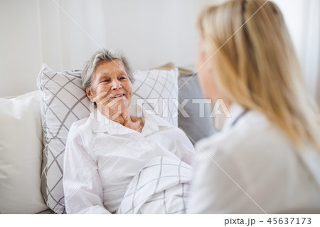 A health visitor talking to a sick senior woman lying in bed at home. A health visitor talking to a sick senior woman lying in bed at home. 45637173
