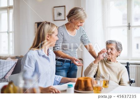 Senior woman in wheelchair with family sitting at the table at home, drinking. 45637235
