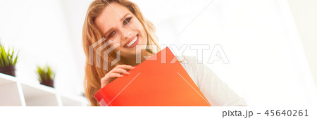 A beautiful young girl stands near a rack in the office and holds a folder with documents. A beautiful young girl stands near a rack in the office and holds a folder with documents. 45640261