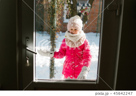 Seven-year-old cute girl in winter clothes is standing outside the door, on the street with snow in Seven-year-old cute girl in winter clothes is standing outside the door, on the street with snow in 45642247