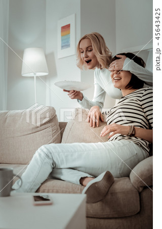 Fascinated blond girl closing eyes of her unsuspecting girlfriend Fascinated blond girl closing eyes of her unsuspecting girlfriend 45643425