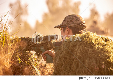 Sniper armed with large caliber, sniper rifle, shooting enemy targets on range from shelter, sitting 45643484
