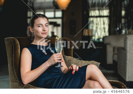 Fashionable gorgeous girl in a dark blue dress drinking cocktail in a luxery hotel lobby bar 45646576