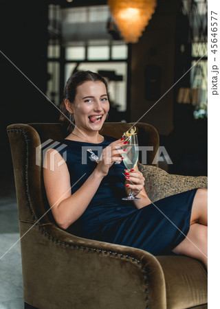 Fashionable gorgeous girl in a dark blue dress drinking cocktail in a luxery hotel lobby bar Fashionable gorgeous girl in a dark blue dress drinking cocktail in a luxery hotel lobby bar 45646577