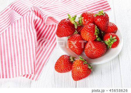 Fresh ripe strawberries on a plate. White wooden table, napkin in red and white stripes. Fresh ripe strawberries on a plate. White wooden table, napkin in red and white stripes. 45658626