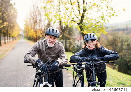 Active senior couple with electrobikes standing outdoors on a road in nature. Active senior couple with electrobikes standing outdoors on a road in nature. 45663711