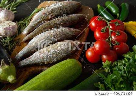 fresh raw dorada fish on a wooden board with a set of vegetables on a black table 45671234