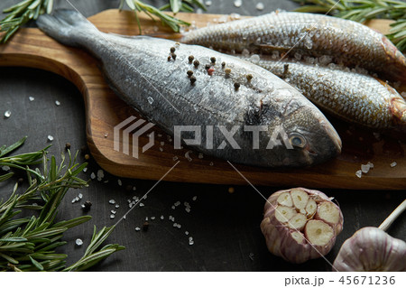 fresh raw dorada fish on a wooden board with a sprig of rosemary and garlic on a black table 45671236