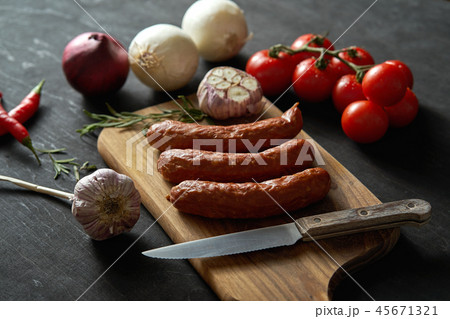 delicious sausages with different vegetables on a wooden board, knife on a black table delicious sausages with different vegetables on a wooden board, knife on a black table 45671321