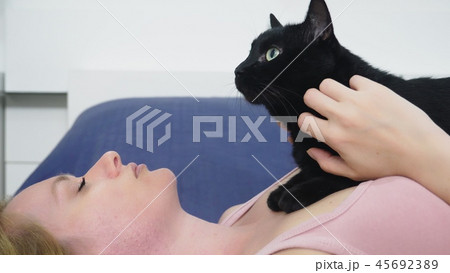Girl with a cat. Beautiful blonde girl lying in bed and caressing her black cat. Caring for animals Girl with a cat. Beautiful blonde girl lying in bed and caressing her black cat. Caring for animals 45692389