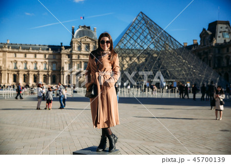 A young girl in a brown coat and scarf stands on the background of city Paris. Autumn is sunny 45700139