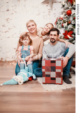Photo of happy family sitting with box with gift at decorated New Year tree 45700668