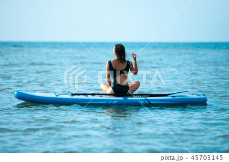 Happy beautiful young girl with paddle board on beach. Blue sea in the background. Summer vacation 45703145