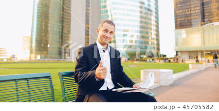 Businessman reading newspaper and looking at watch outside, . Businessman reading newspaper and looking at watch outside, . 45705582