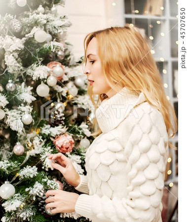 woman in white sweater stands near a Christmas tree woman in white sweater stands near a Christmas tree 45707650