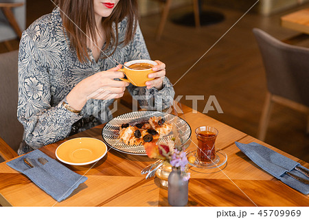 Young woman drinking coffee. Female holding cup. Sitting in coffee shop at wooden table. On table Young woman drinking coffee. Female holding cup. Sitting in coffee shop at wooden table. On table 45709969