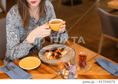Young woman drinking coffee. Female holding cup. Sitting in coffee shop at wooden table. On table Young woman drinking coffee. Female holding cup. Sitting in coffee shop at wooden table. On table 45709979
