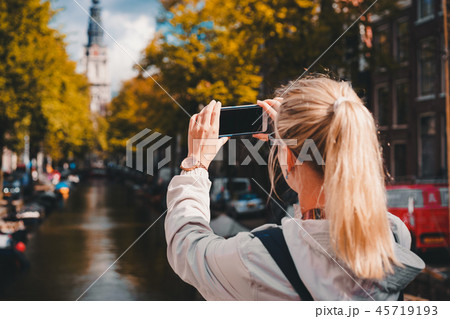 Woman tourist taking a picture of canal in Amsterdam on the mobile phone. Warm gold afternoon Woman tourist taking a picture of canal in Amsterdam on the mobile phone. Warm gold afternoon 45719193