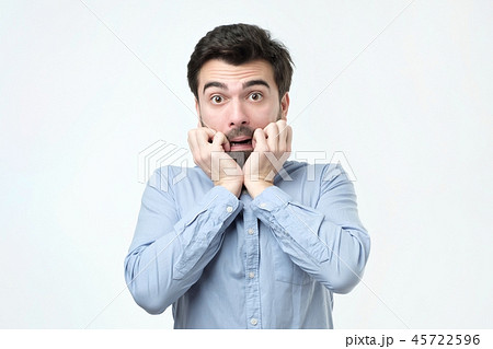 Young man dressed in casual clothes, biting nails and rounding eyes 45722596