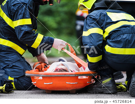 Firefighters putting an injured woman into a plastic stretcher after a car accident. Firefighters putting an injured woman into a plastic stretcher after a car accident. 45726814