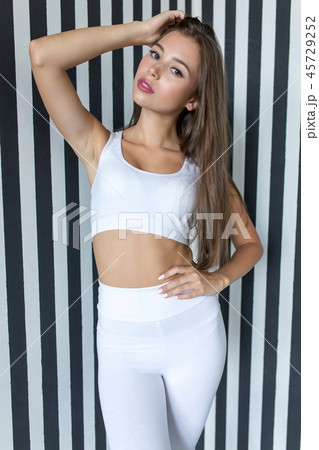 Attractive young woman in white sports top and leggings on striped background. Attractive young woman in white sports top and leggings on striped background. 45729252