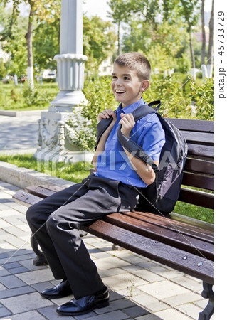 Brunette boy sitting on bench with school backpack 45733729