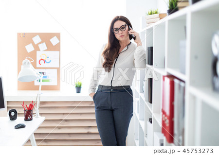 A young girl standing near the rack with documents and holding a phone. A young girl standing near the rack with documents and holding a phone. 45753273