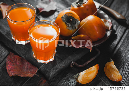 Ripe orange persimmon fruit and persimmon leaves in a brown plate on a black wooden table 45766725