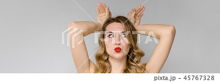 A young beautiful girl fools by putting two hands on her head and twisting her face. Funny portrait 45767328