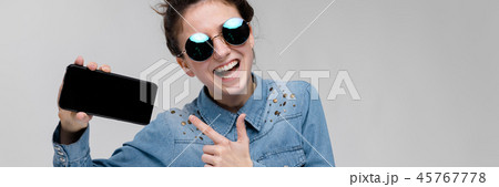 Young brunette girl in round glasses. Hairs are gathered in a bun. Girl with a black phone. Young brunette girl in round glasses. Hairs are gathered in a bun. Girl with a black phone. 45767778