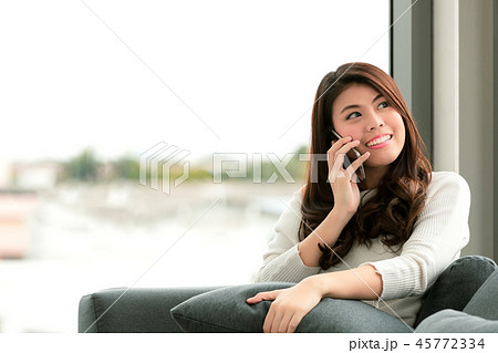 Asian woman in a casual dress is sitting on sofa near big glass 45772334