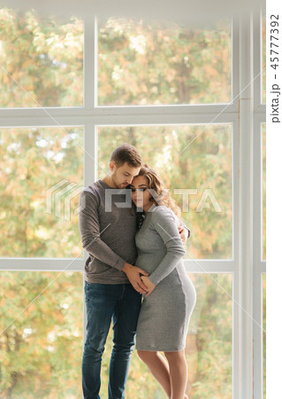 Man hug his pregnant wife and put his hand on her belly. They stand near the window Man hug his pregnant wife and put his hand on her belly. They stand near the window 45777392