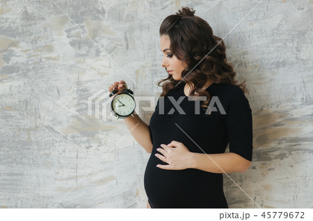 Portrait of beautiful pregnant woman in black bodysuit. She hold the clock in hands symbolic hinting Portrait of beautiful pregnant woman in black bodysuit. She hold the clock in hands symbolic hinting 45779672