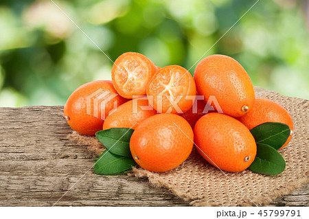 Cumquat or kumquat with leaf on old wooden table with blurry garden background Cumquat or kumquat with leaf on old wooden table with blurry garden background 45799791