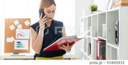 A young girl in the office talking on the phone and holding a folder with documents. A young girl in the office talking on the phone and holding a folder with documents. 45800932