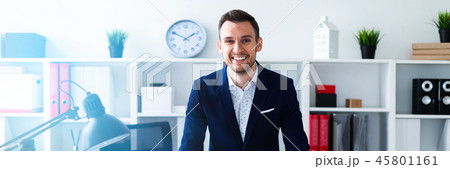 A young man stands in the office near the table and puts his hands on him. 45801161