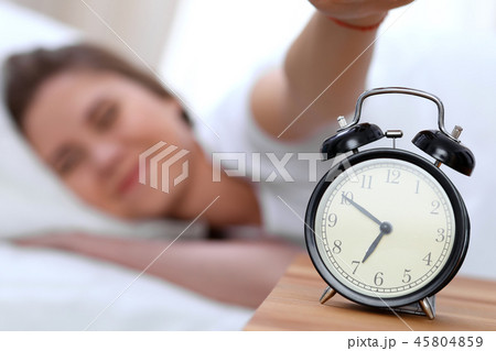 Alarm clock opposite of sleepy young woman stretching hand to ringing alarm willing turn it off 45804859