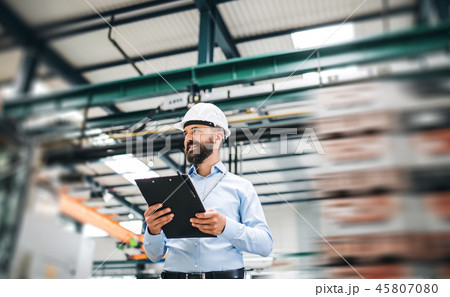 A portrait of an industrial man engineer with clipboard standing in a factory. A portrait of an industrial man engineer with clipboard standing in a factory. 45807080