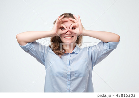 Pretty girl with surprised face holding fingers near eyes like glasses: mask like super hero or owl Pretty girl with surprised face holding fingers near eyes like glasses: mask like super hero or owl 45815203