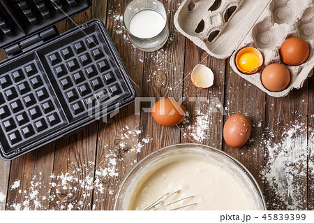 Making waffles at home - waffle iron, batter in bowl and ingredients - milk, eggs and flour. Making waffles at home - waffle iron, batter in bowl and ingredients - milk, eggs and flour. 45839399