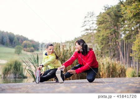 Two female runners stretching legs outdoors in park in autumn nature. Two female runners stretching legs outdoors in park in autumn nature. 45841720