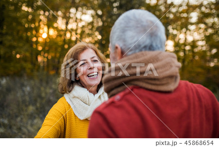 A senior couple standing in an autumn nature at sunset, looking at each other. A senior couple standing in an autumn nature at sunset, looking at each other. 45868654