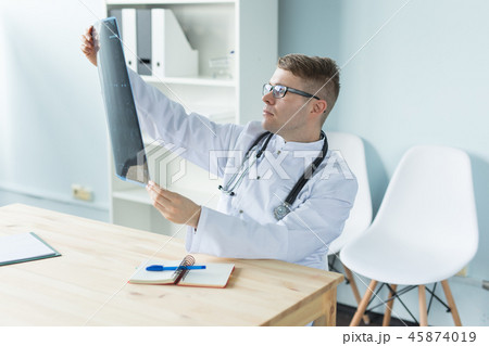 Healthcare, medical and people concept - doctor examines an x-ray sitting behind a desk Healthcare, medical and people concept - doctor examines an x-ray sitting behind a desk 45874019
