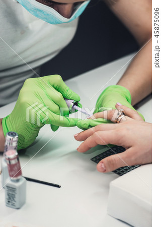 Professional manicure master in green gloves making manicure in salon 45875096