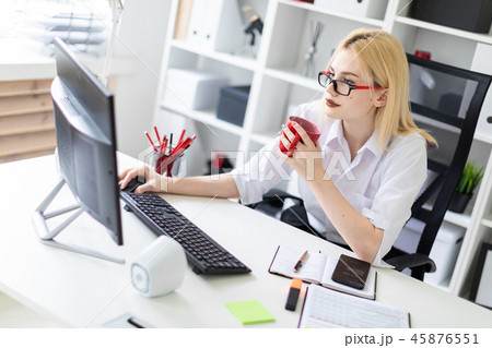 A young girl working at a computer in the office and holding a red Cup. A young girl working at a computer in the office and holding a red Cup. 45876551